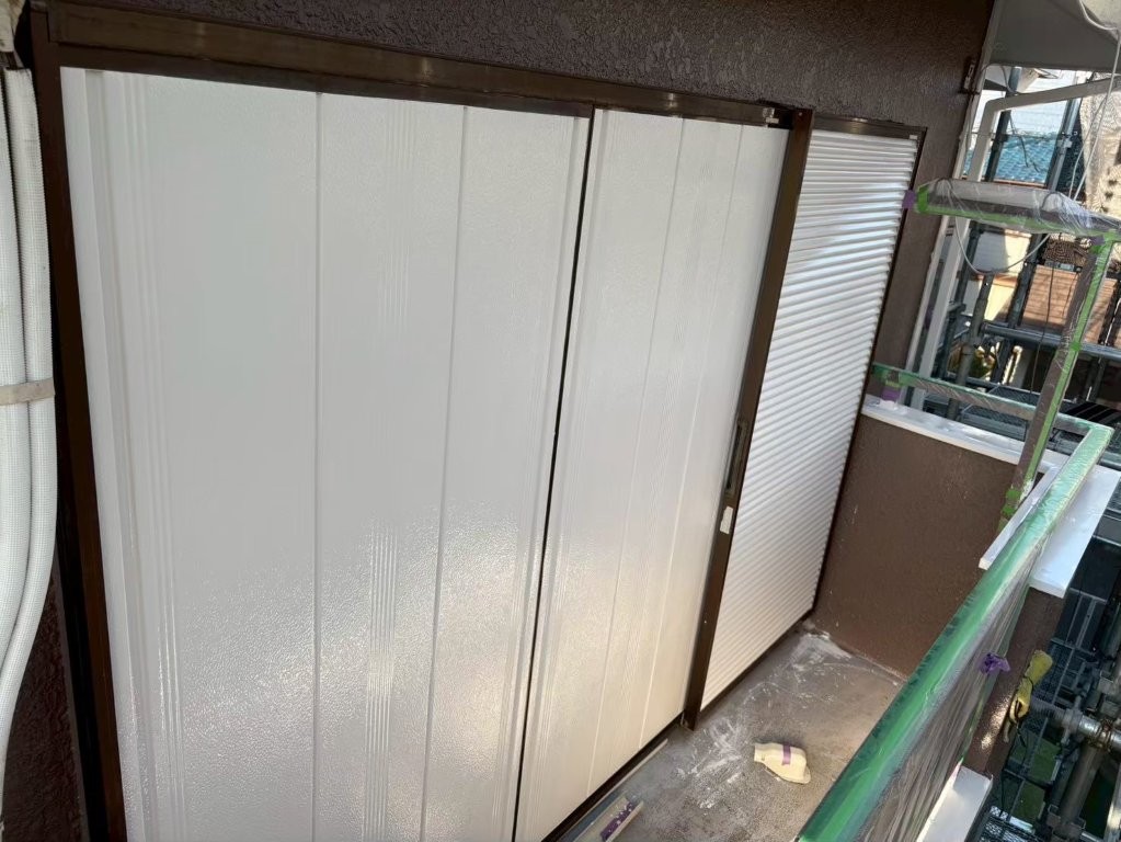 中塗り塗装が完了した雨戸全体の様子。外壁と調和するホワイト系の仕上がりで、ベランダ周辺の印象も明るく変化。