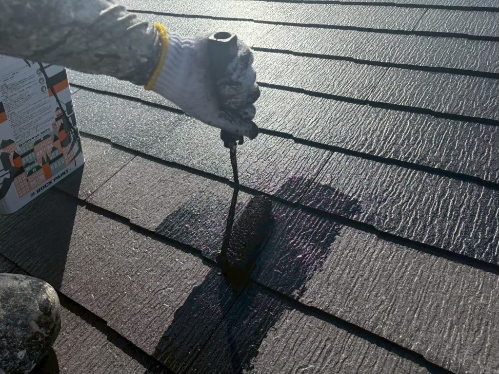 千葉市若葉区S様邸のスレート屋根にローラーで中塗り塗装（主材1回目）を施工している様子。屋根材の凹凸に塗料を丁寧に浸透させている工程。